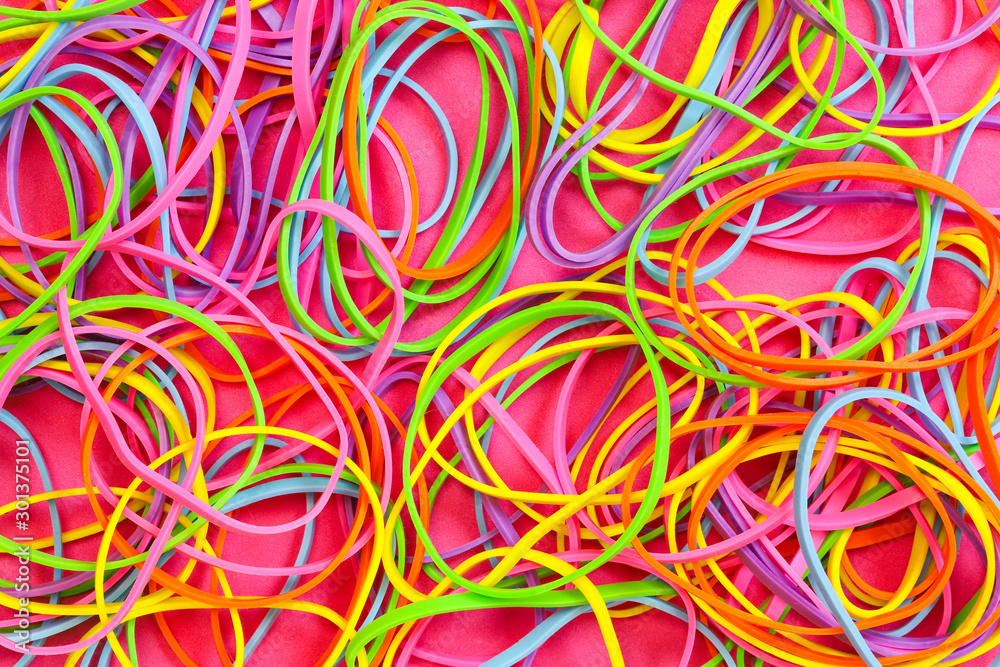 A pile of neon colored elastic rubber bands against a pink background