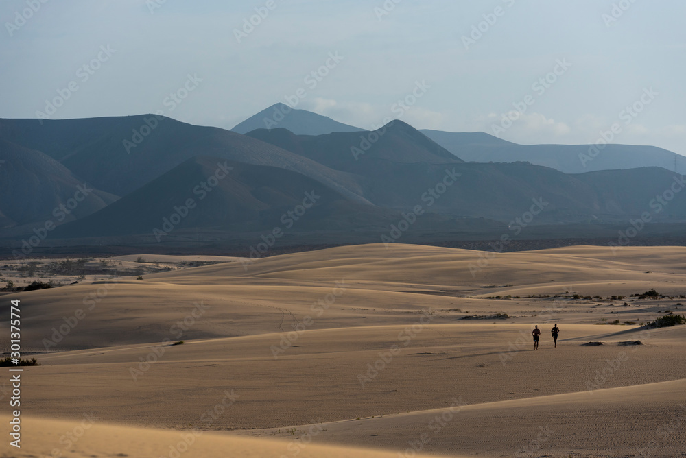 Dos hombres corriendo sobre las dunas del desierto con las montañas al fondo. Dos hombres corriendo sobre las dunas del desierto con las montañas al fondo.