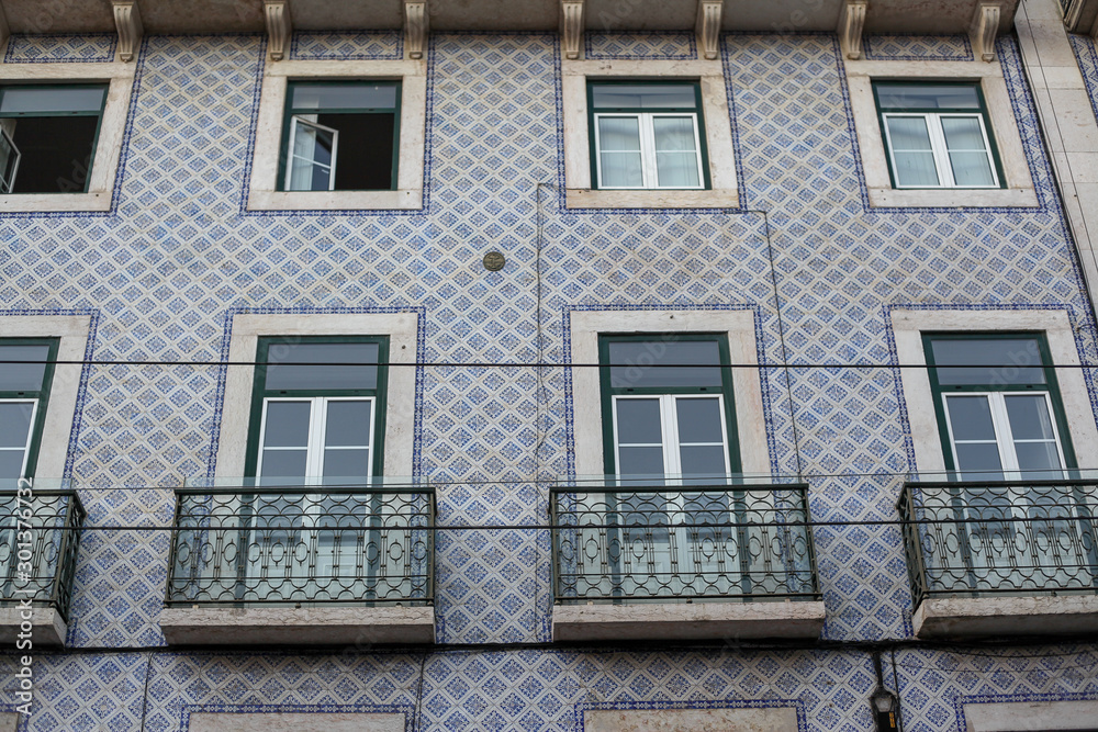 A beautiful architecture of the traditional tiled walled facade with large glass doors and windows and the iron balcony in the city of Lisbon in Portugal