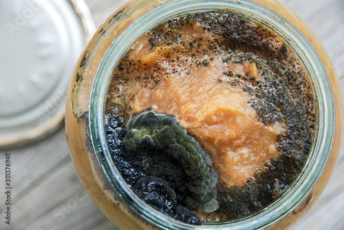 Open glass jar of homemade apple jam with dark mold on top. Improper storage of home canned food. photo