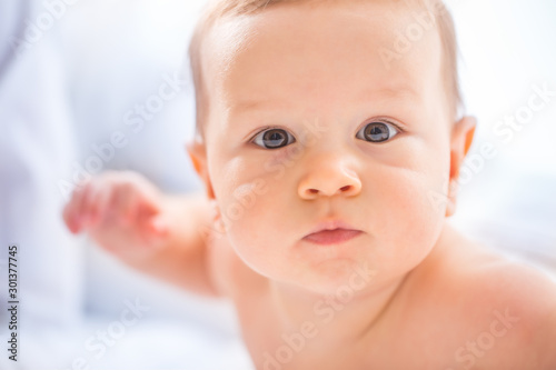 Portrait of cute toddler boy lying on bed. Newborn child in bedroom. Baby lies on his tummy and raises the head