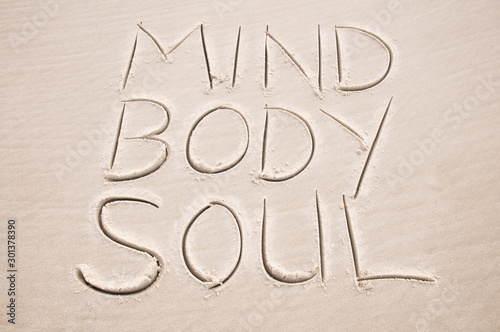 Holistic health message handwritten in smooth sand spelling out Mind Body and Soul on the beach photo