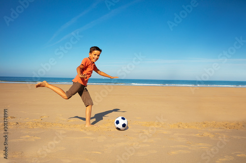 Little boy play soccer on the sand sea beach