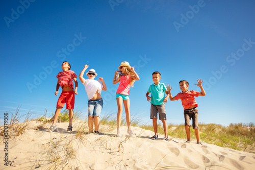 Group of kids dance on sand beach dune together