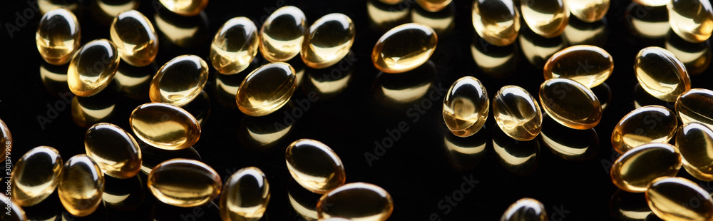 shiny golden fish oil capsules scattered on black background, panoramic shot