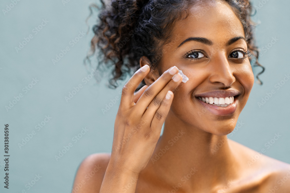 Woman applying moisturizer on face - obrazy, fototapety, plakaty 