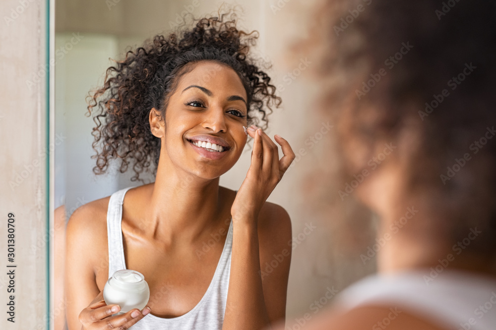 Black girl applying lotion on face - obrazy, fototapety, plakaty 