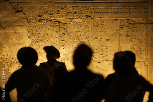 Group of unrecognizable tourist archeologists standing in silhouette in front of ancient Egyptian hieroglyphs photo