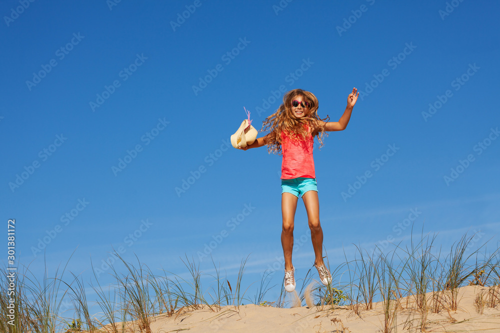 Happy girl jump high on the sand dune holding hat Happy girl jump high on the sand dune holding hat