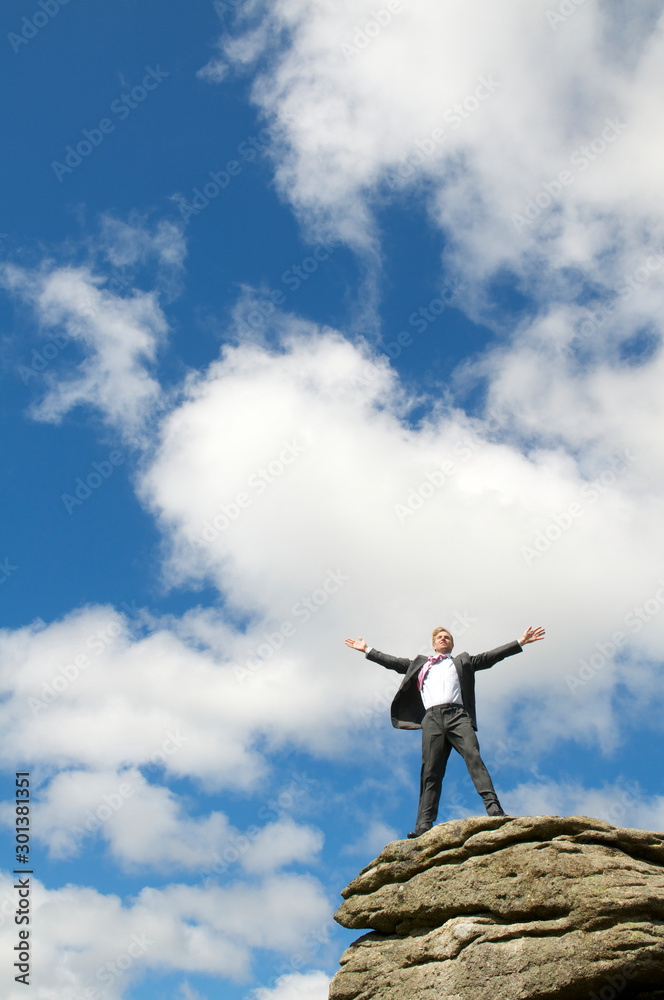 Proud businessman standing with his arms spread on a windblown rocky mountaintop Proud businessman standing with his arms spread on a windblown rocky mountaintop