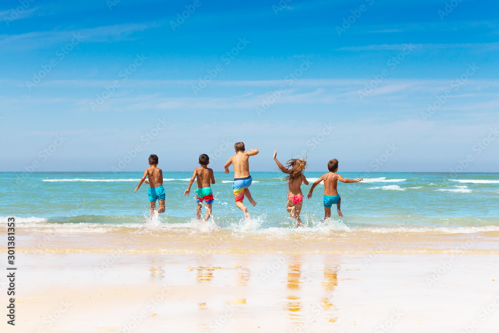 Many kids friends run into sea waves on sand beach
