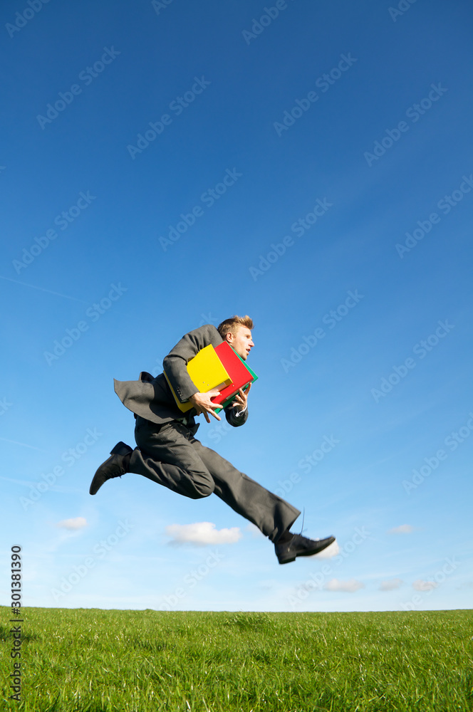 Businessman takes a flying leap with file folders above a bright green meadow Businessman takes a flying leap with file folders above a bright green meadow