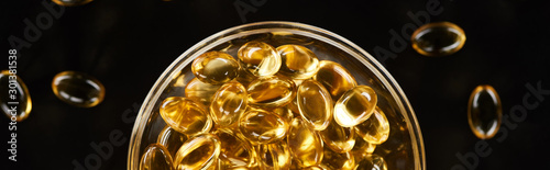 top view of golden fish oil capsules in glass bowl isolated on black  panoramic shot