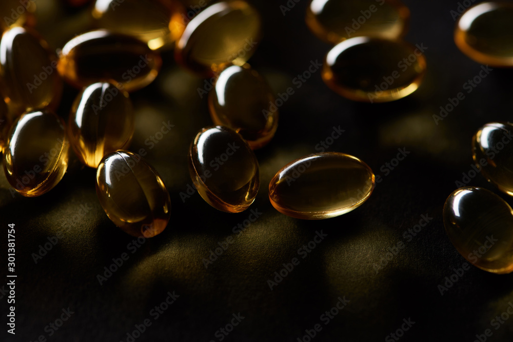 close up view of golden fish oil capsules on black background in dark close up view of golden fish oil capsules on black background in dark
