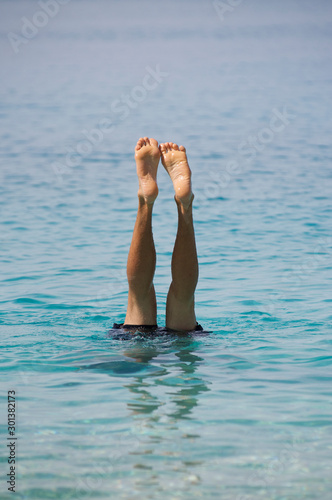 Bare feet of unrecognizable man doing underwater headstand sticking up out of rippling blue waters photo