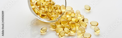 golden fish oil capsules in glass bowl on white background, panoramic shot photo
