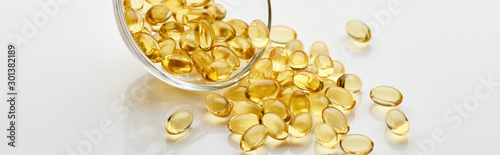 Slika na platnu golden fish oil capsules in glass bowl on white background, panoramic shot