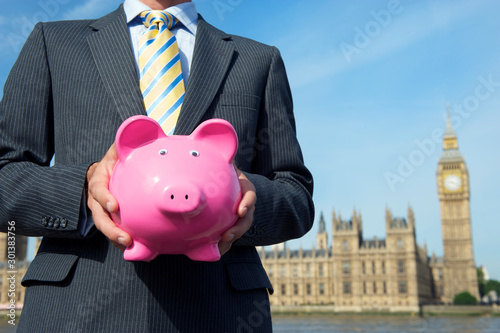 British politician holding a classic pink piggy bank in front of the Houses of Parliament in London, UK photo