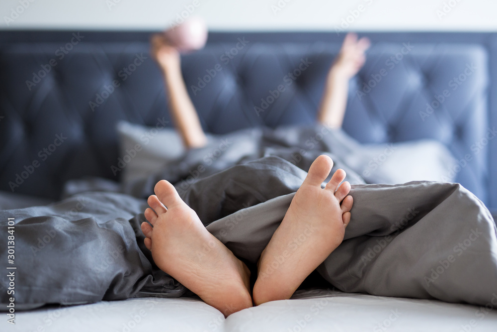 good morning concept - female hands and legs sticking out from the blanket - obrazy, fototapety, plakaty 