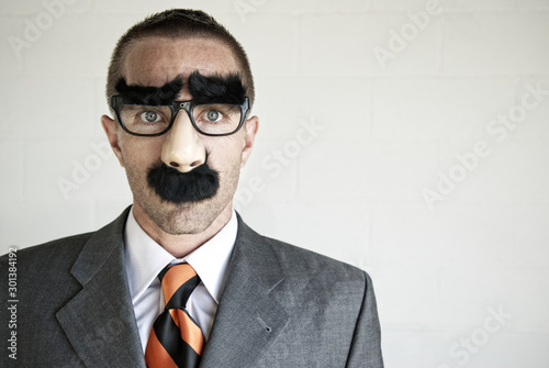 Businessman hiding his identity wearing a disguise of glasses with thick eyebrows and mustache looking at camera with blank expression