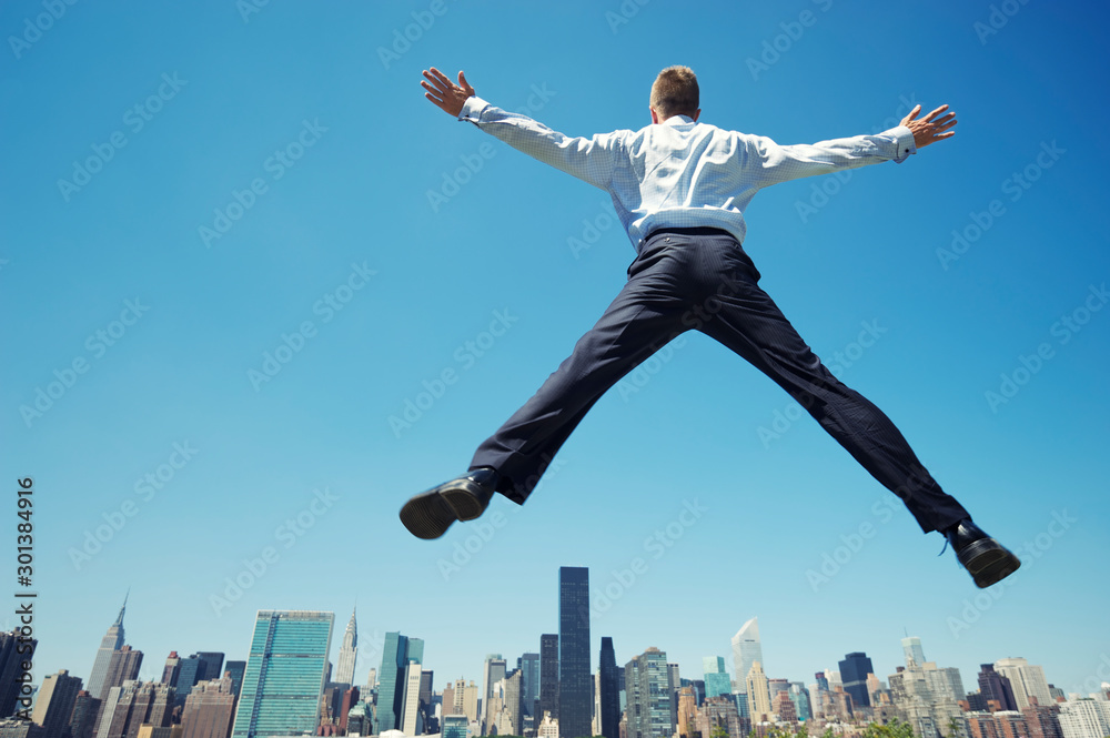 Giant businessman doing a spreadeagle jump outdoors in a blue sky celebration above the city skyline Giant businessman doing a spreadeagle jump outdoors in a blue sky celebration above the city skyline
