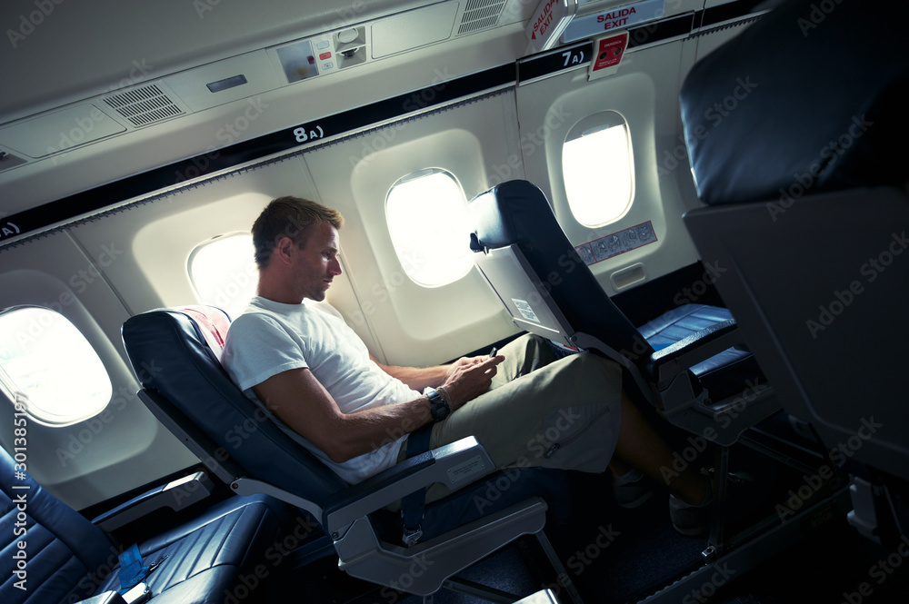 Young traveling man sitting on small airplane texting on smartphone during takeoff