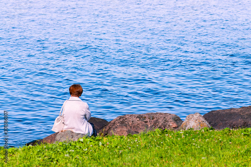 woman in white sits on a stone on the shore
