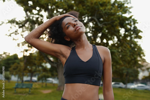 Portrait of a fit young black woman stretching her neck in the park before doing exercise outdoors