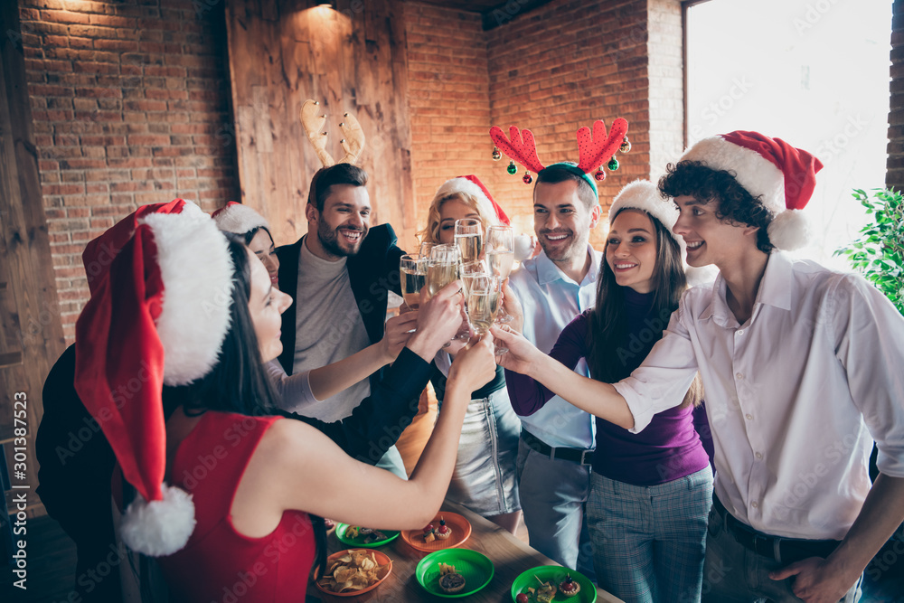 Obraz premium Photo of group meeting x-mas party many people celebrating clinking wineglasses drink sparkling wine wear formalwear santa hats deer horns standing around table indoors
