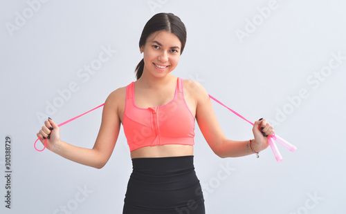 Young asian girl is standing next to gray background is smiling and holding jump rope.