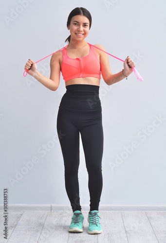 Young asian girl is standing next to gray background is smiling and holding jump rope