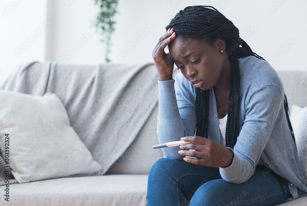Depressed black girl holding pregnancy test, upset with positive result - obrazy, fototapety, plakaty 