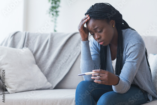 Depressed black girl holding pregnancy test, upset with positive result