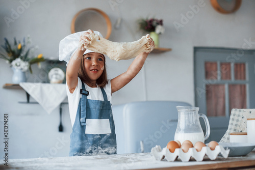 Cute kid in white chef uniform preparing food on the kitchen