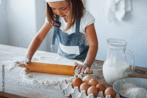 Cute kid in white chef uniform preparing food on the kitchen photo