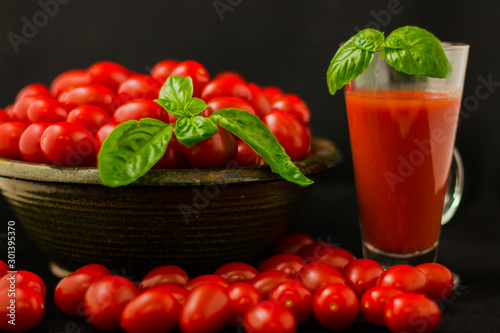 CHERY TOMATOES ON BLACK BACKGROUND WITH BASIL AND JUICE WITH SELECTIVE FOCUS