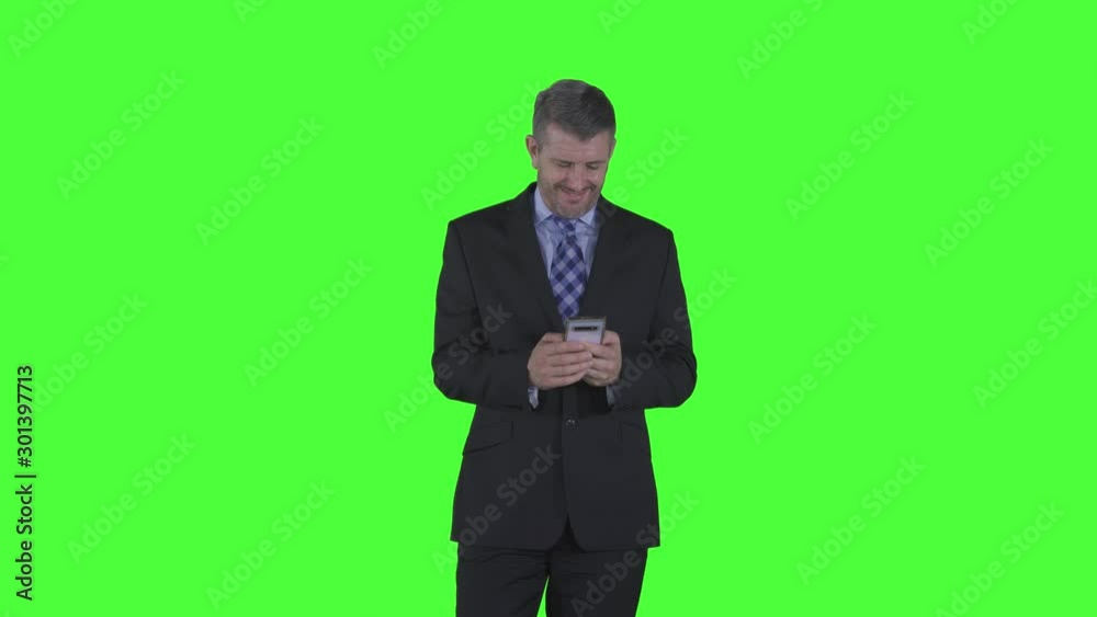 Happy caucasian businessman using a mobile phone while smiling and standing in the studio. Shot in 4k resolution with green screen background Happy caucasian businessman using a mobile phone while smiling and standing in the studio. Shot in 4k resolution with green screen background