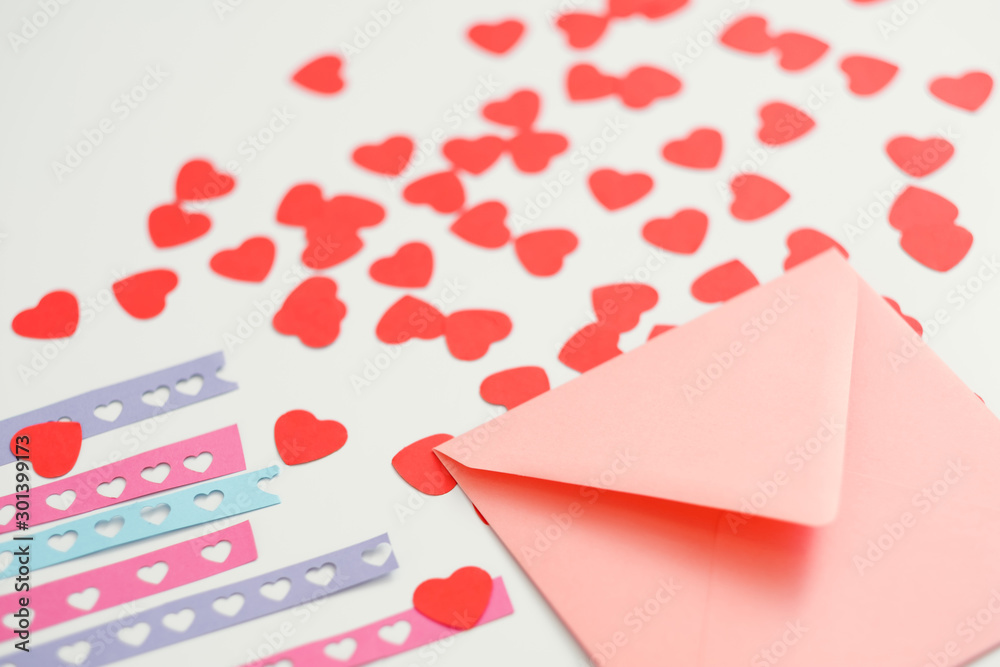 Handmade greeting card. Closeup of pink envelope, love theme stencil plates and cutout paper hearts on white background.
