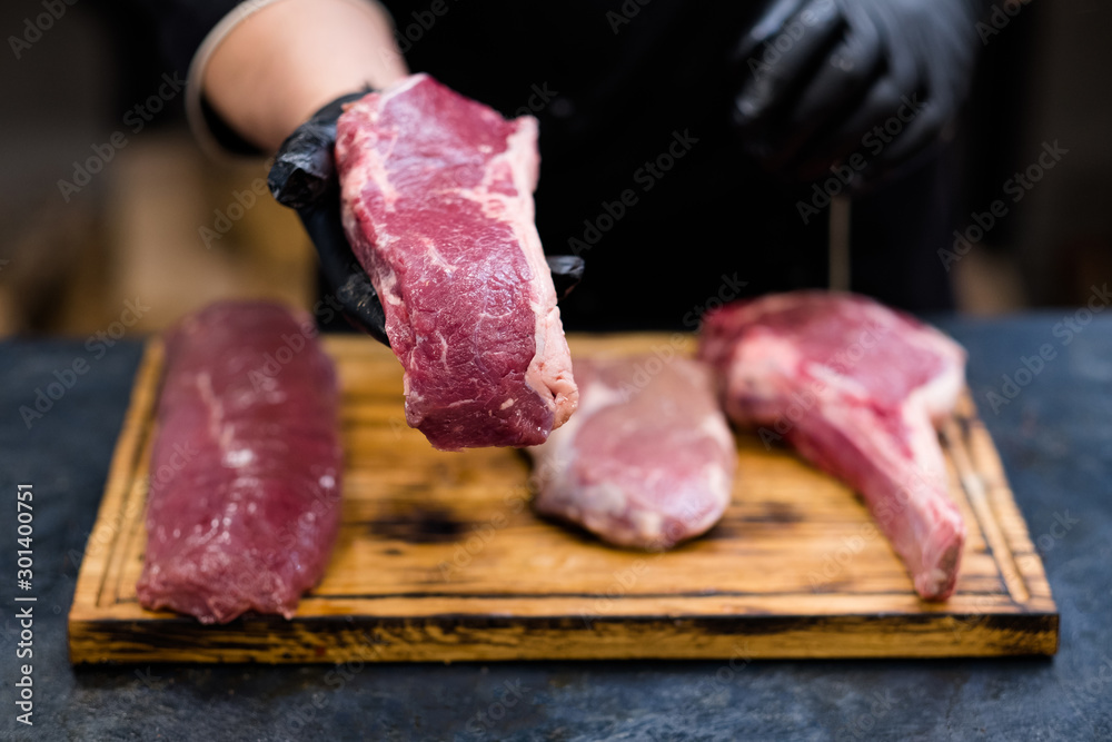 Butcher shop. Fresh cuts, raw beef meat assortment on wooden board. Chef cooking steaks.