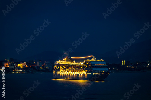 Big cruise ship with festive night lights stopped for the night in the bay near the sea port of Saranda, Albania. Albanian mountains and Saranda town in the background.