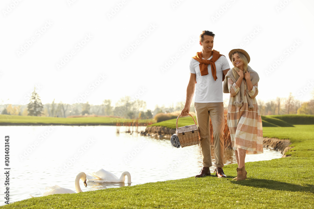 Obraz premium Young couple with picnic basket near lake on sunny day