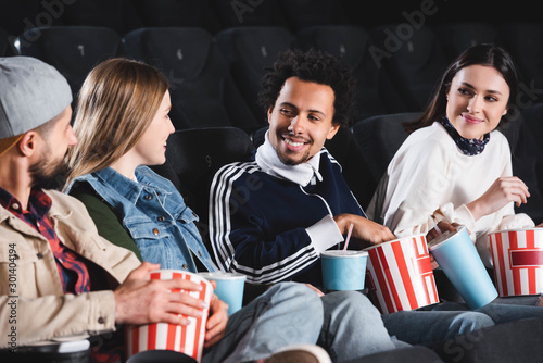 multicultural friends sitting, smiling and talking in cinema