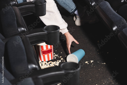 cropped view of woman taking paper cup with soda from floor in cinema