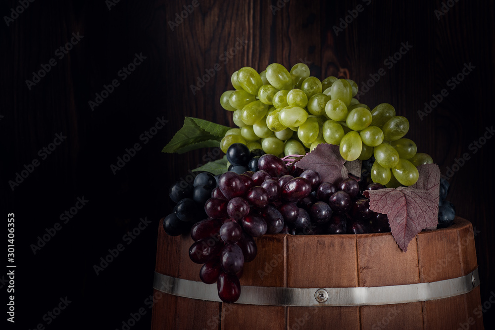 Harvested red and white grapes in a cellar on a barrel.