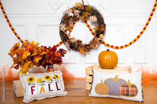 Festive fall decoration with leaves, wreath, garland, pumpkin, crate, pillows, and tulle for homes or photo shoots