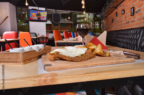 CLASSIC BREADED FRIED MEAT , KNOWN IN ARGENTINA AS MILANESA, TWO SUNNY SIDE UP EGGS, SERVED WITH FRENCH FRIES ON A WOODEN TABLE