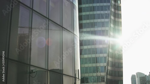 Beautiful lens flare through Skyscrapers with green and blue glass windows at business district in Paris, Side track to right then left, wide shot with reflections. Futuristic modern building.