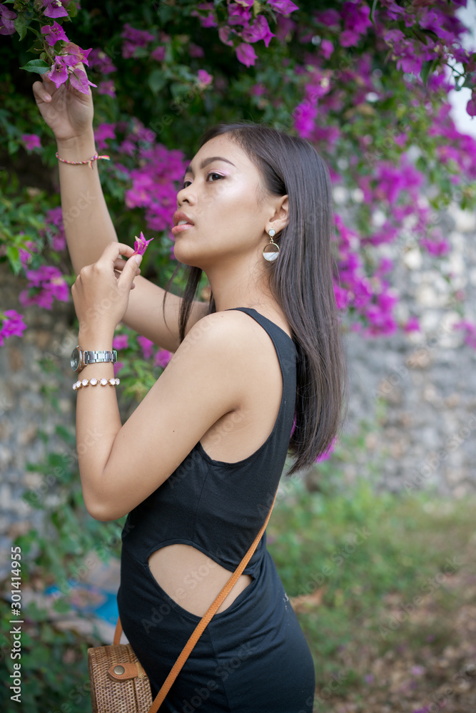 Asian girl. Beautiful Balinese women in black dress collects pink flowers in beautiful garden Asian girl. Beautiful Balinese women in black dress collects pink flowers in beautiful garden
