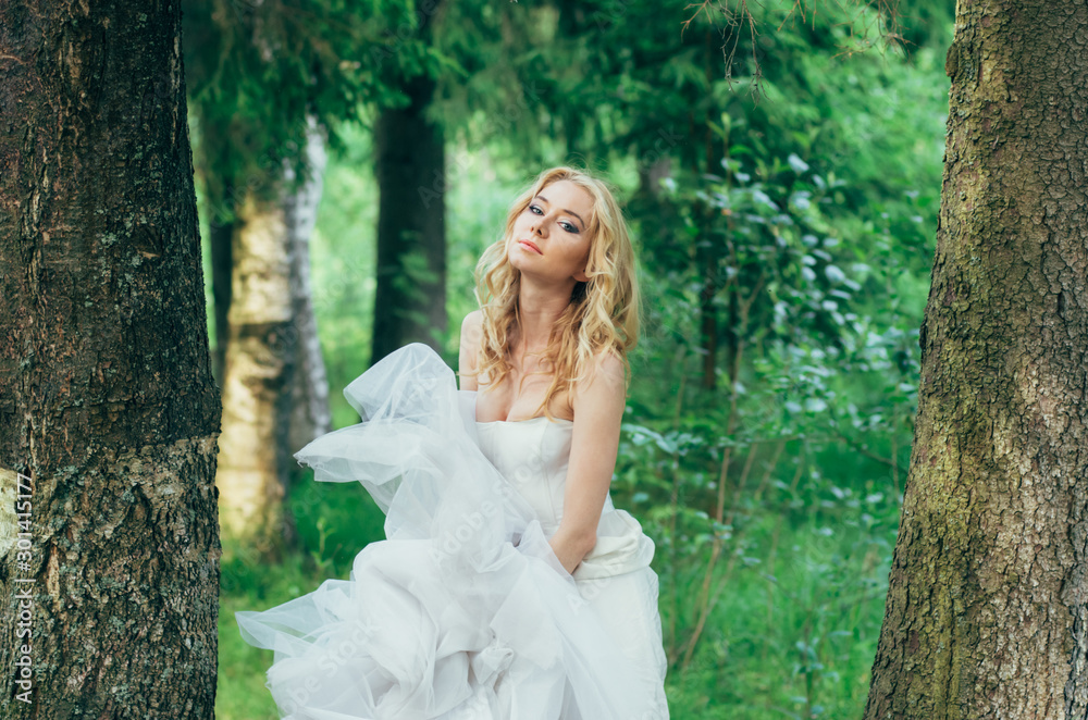 Portrait of young blond bride in forest with dress in hands Portrait of young blond bride in forest with dress in hands