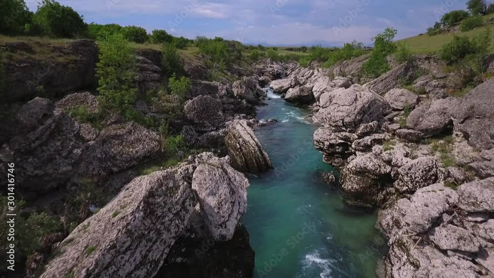 Aerial shot of fast river flow through rocks surrounded by low green vegetation Aerial shot of fast river flow through rocks surrounded by low green vegetation
